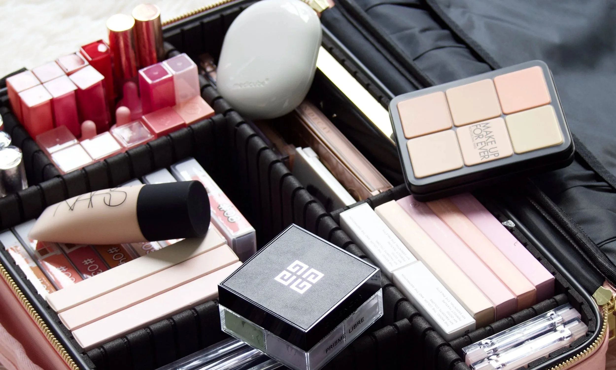A suitcase filled with makeup and skincare products, including lipstick, foundation, and powder.