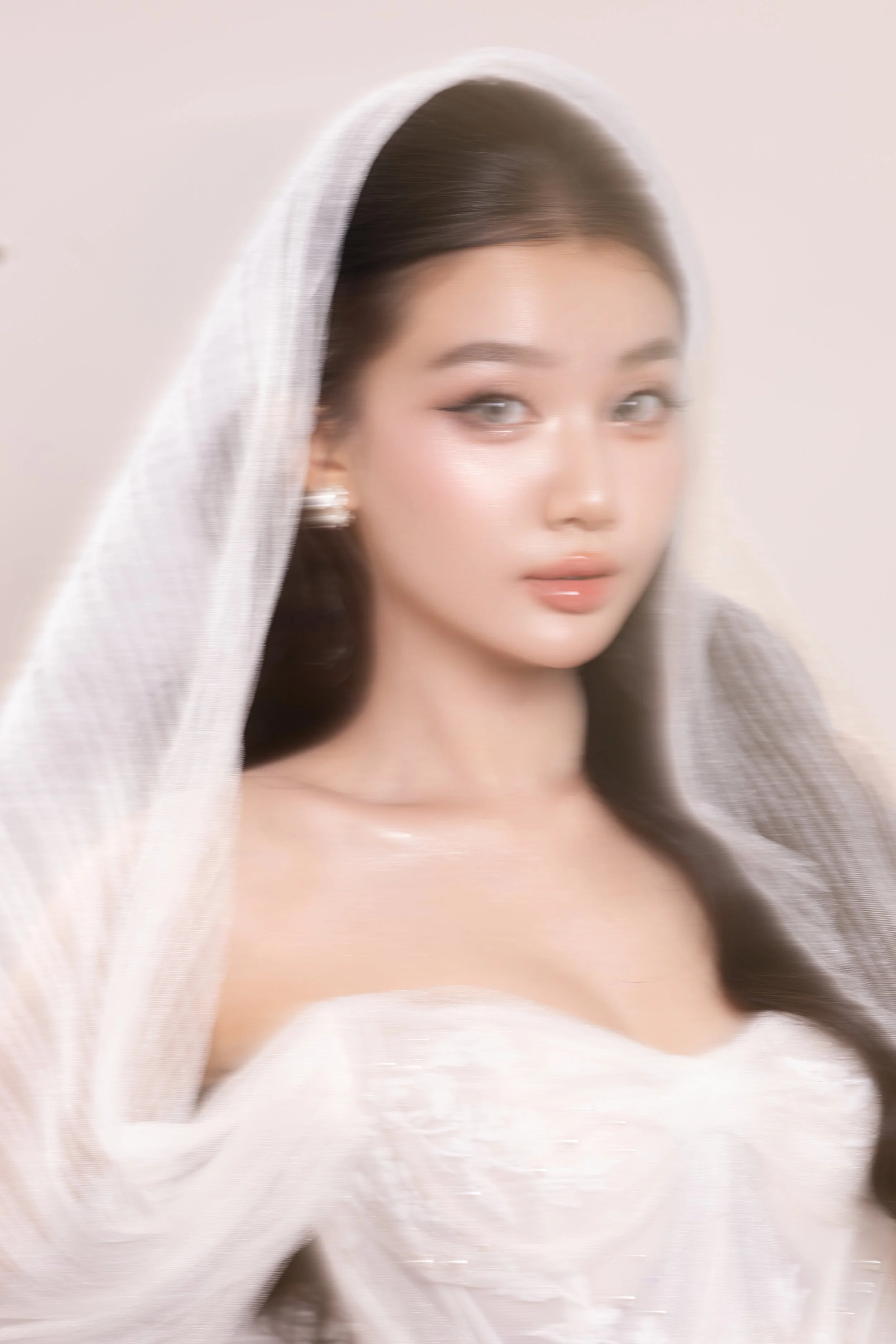A woman dressed in a white wedding gown with a veil over her dark hair, looking at the camera with a soft expression.
