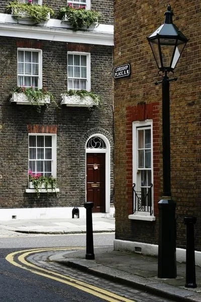 Street corner with brick buildings, black lamp post, and a house with flower boxes in windows, London street sign on brick wall.