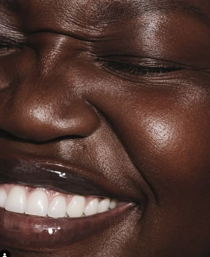 Close-up of a person smiling with white teeth, showing dimples and skin with a rich dark tone.