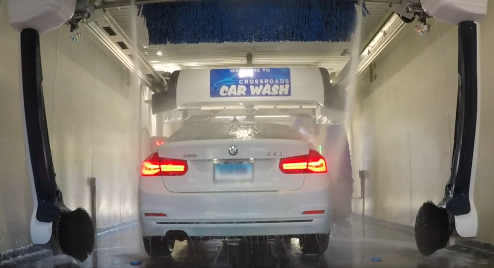 White BMW car inside an automated soft touch car wash, with reverse osmosis treated water beginning the rinse process. Soft touch wash in best to remove: dirt, pollen, road oil film and heavy grime.
