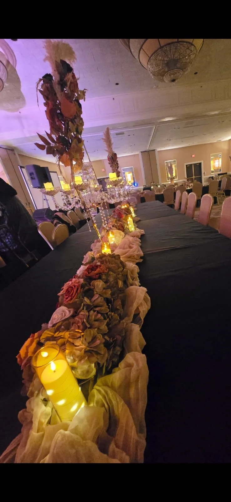 Elegant banquet table decorated with floral centerpieces, candles, and draped fabric in a dimly lit event hall.