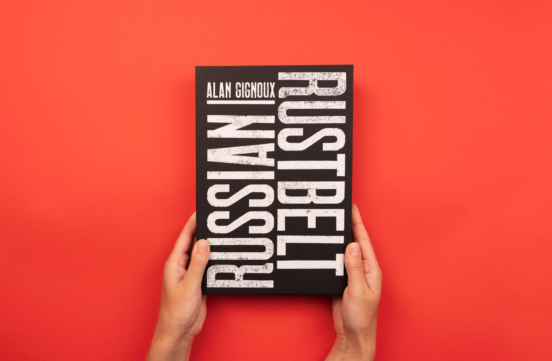 Book titled "Rust Belt" by Alan Gignoux, held by two hands against a red background.