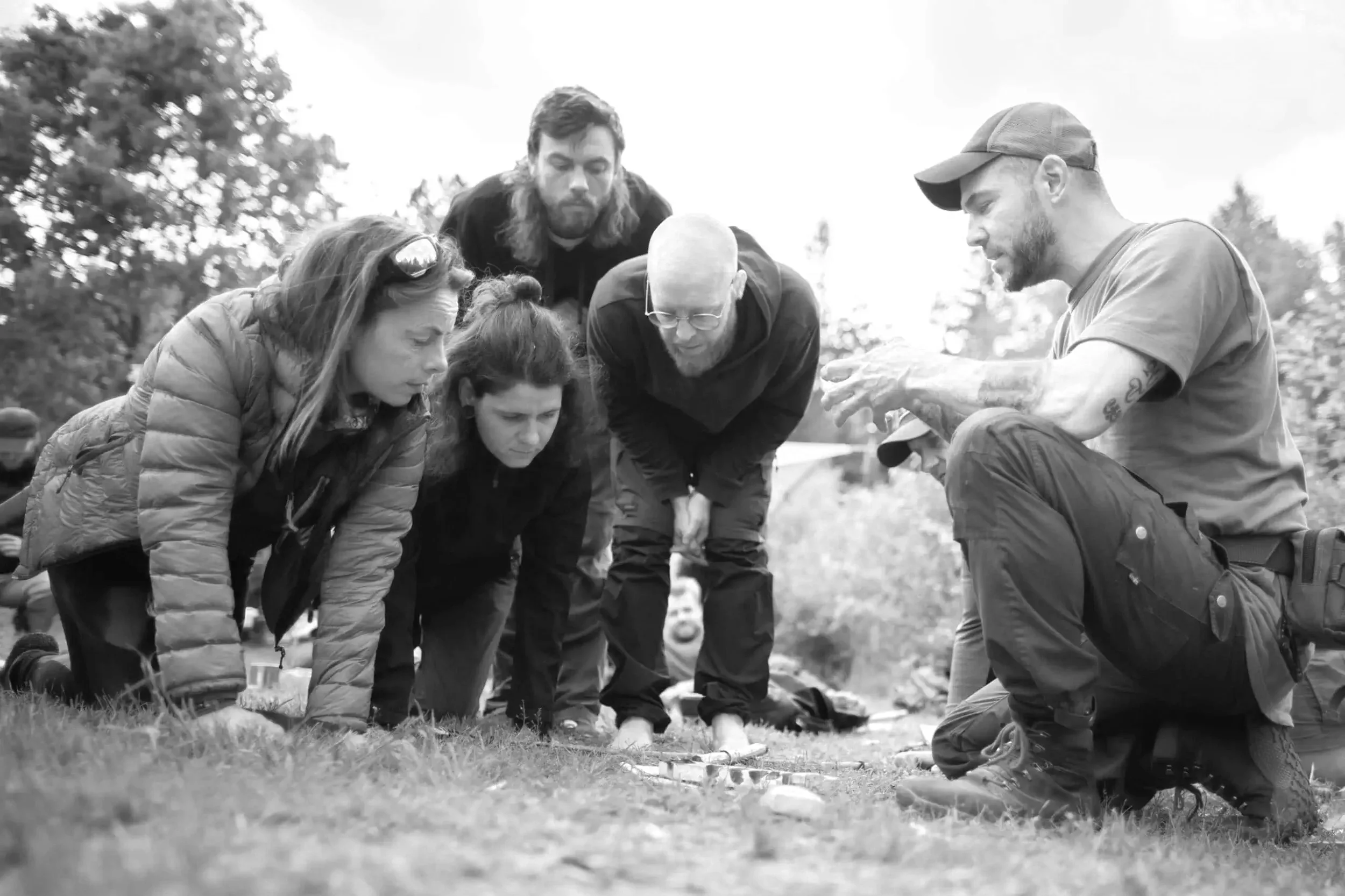 Group of six people kneeling and bending over on grass, engaged in an outdoor activity or lesson.
