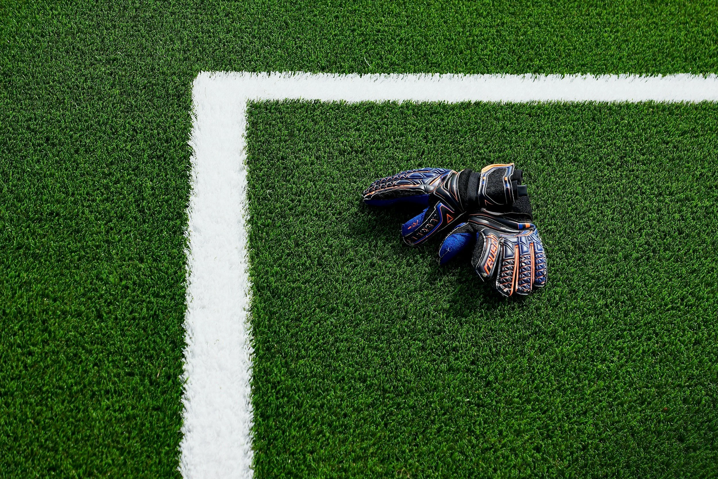 A pair of black and blue goalkeeper gloves resting on a green football field with white lines.