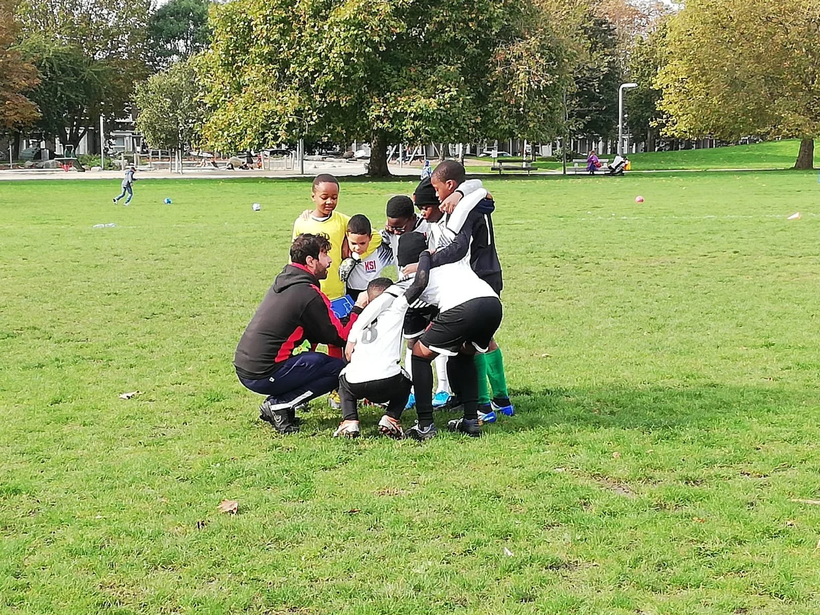 A group of young soccer players with their coach on a grassy field during daytime.