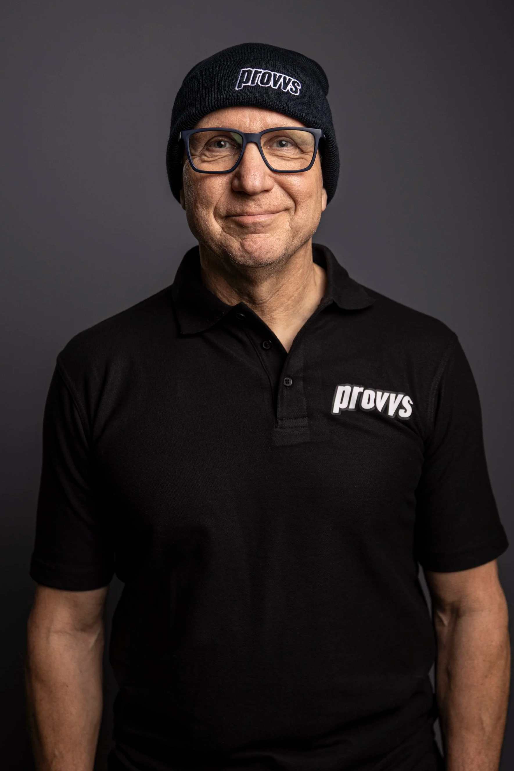 En man med glasögon, svart tröja och mössa med texten 'prouvs'