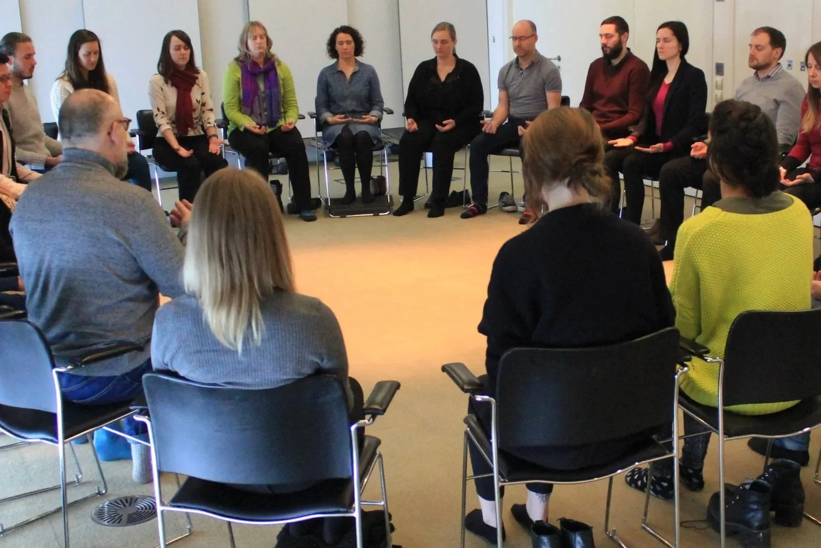 People sitting in a large circle in a conference room, engaged in a meditative or mindfulness activity.