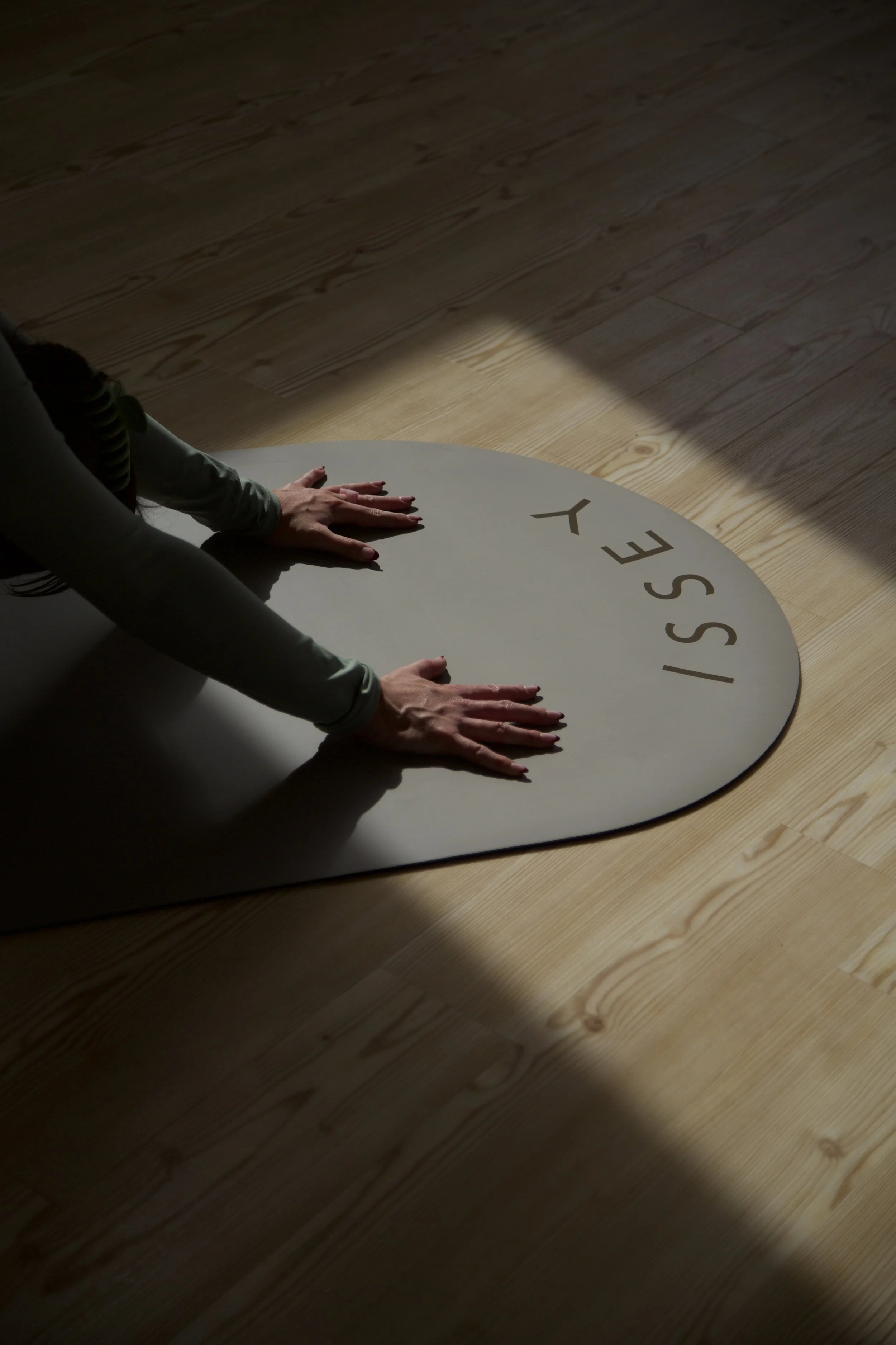 Person doing yoga on a mat with 'SSEY' written on it in a room with wooden floors and sunlight shadows.