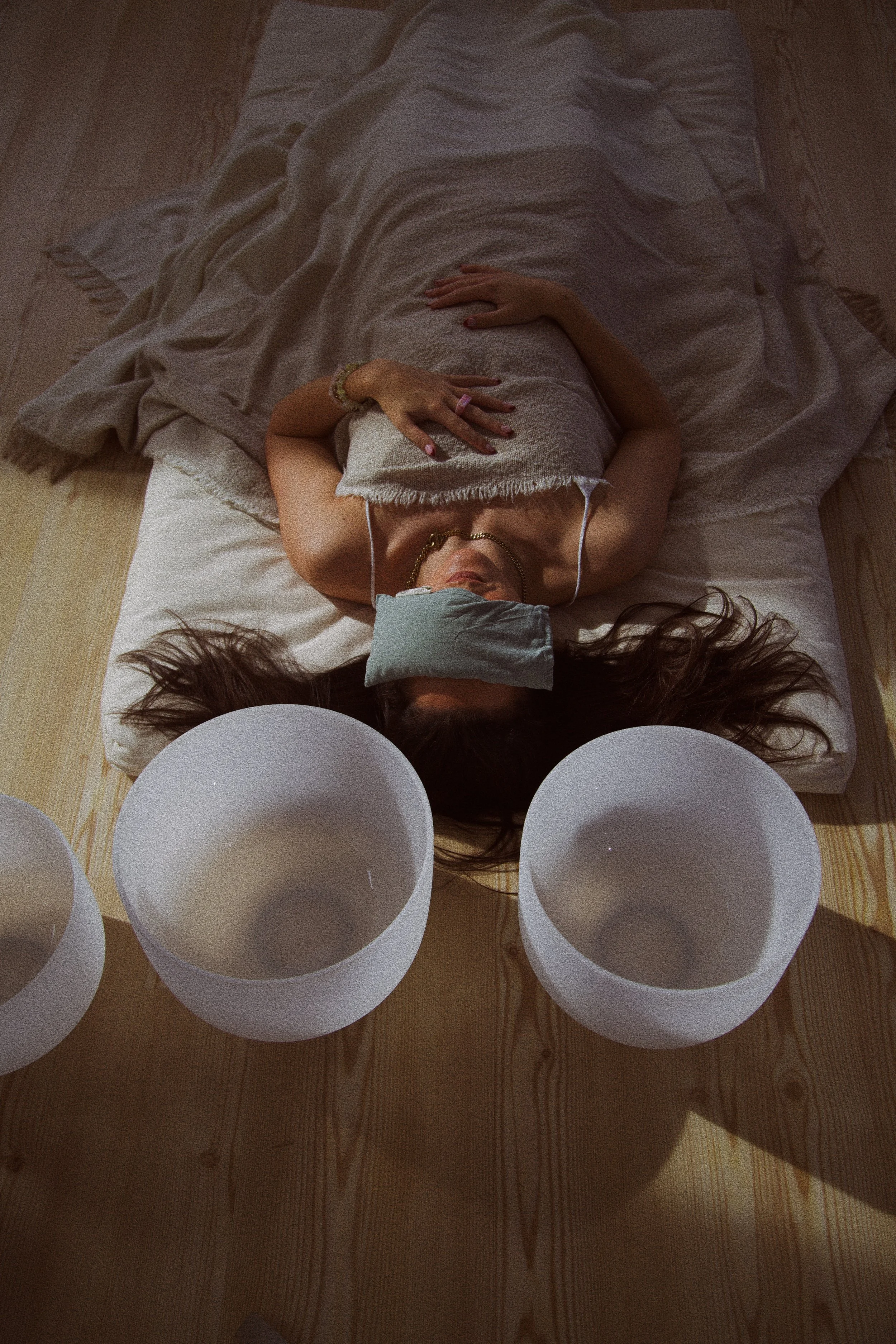 Woman lying on a bed with a pillow over her eyes, surrounded by large empty bowls on a wooden floor.