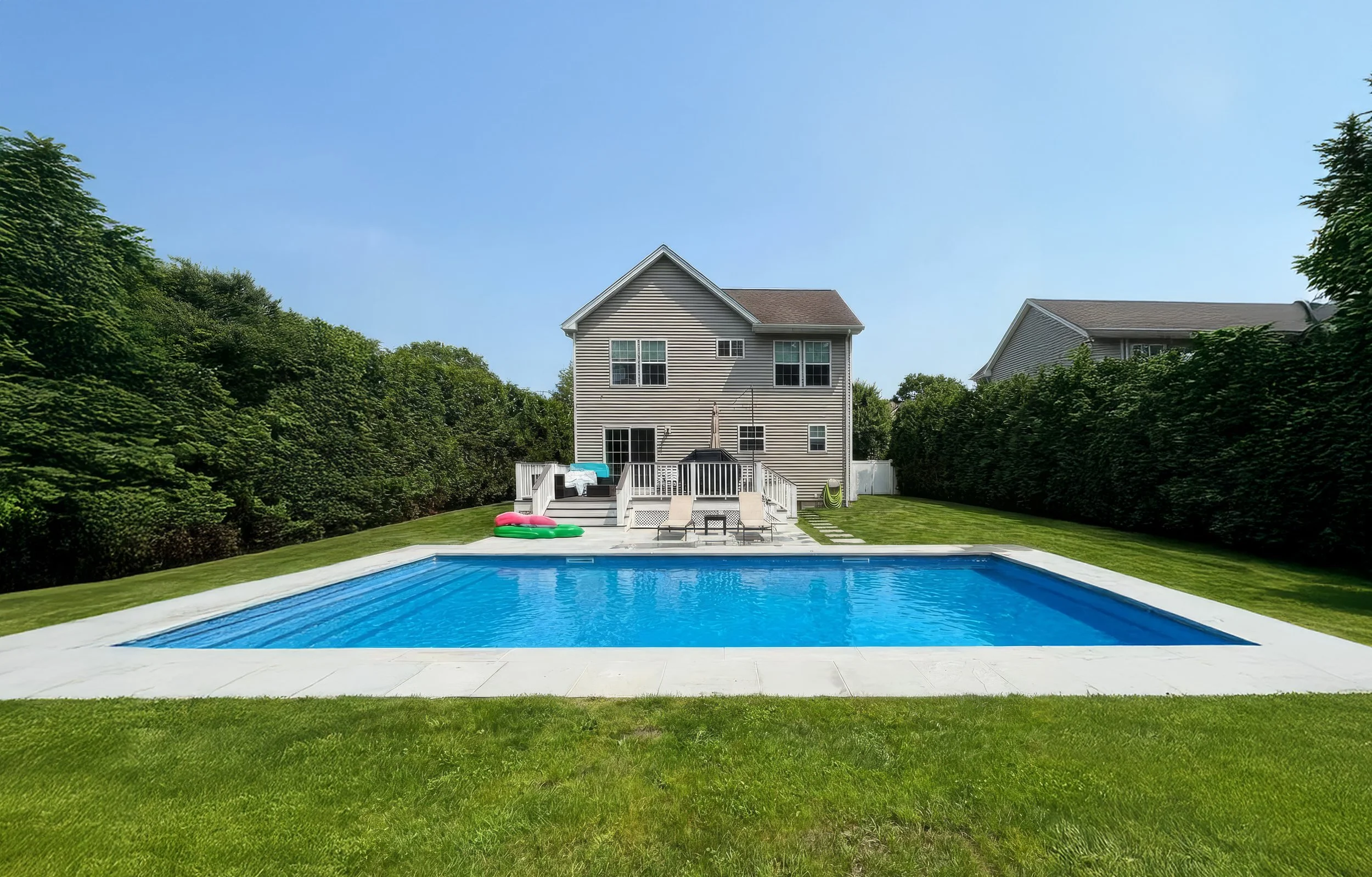 Residential backyard with a swimming pool, lawn, and two-story house on a sunny day.