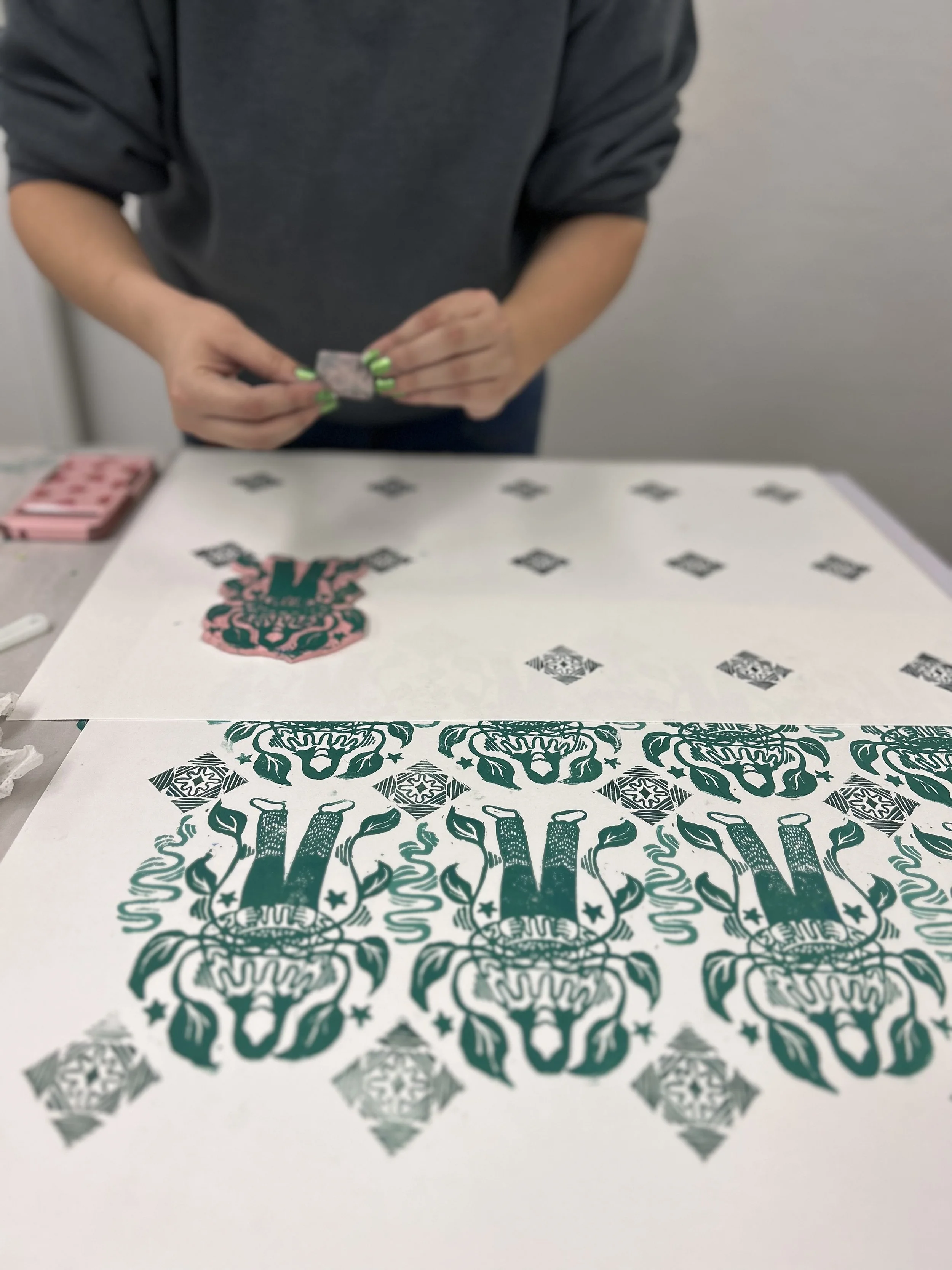 Person working with tattoo stencils on a table, displaying intricate black and green designs, including skull and floral elements.