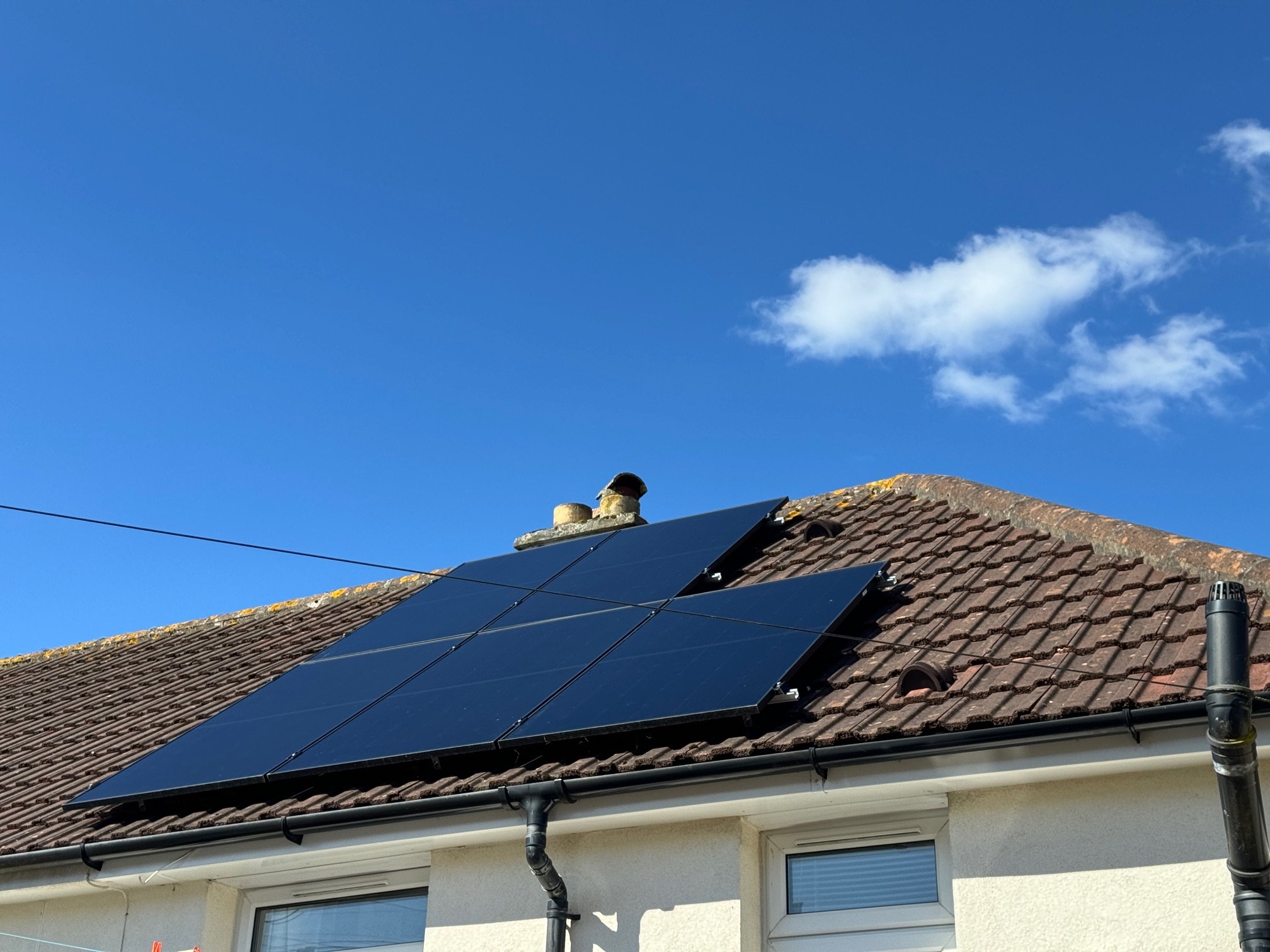 Solar panels installed on the roof of a house against a blue sky with a few clouds.