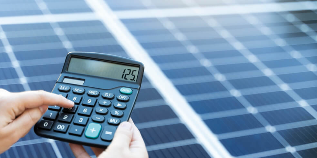 Photovoltaic solar panel with a financial calculator and pencil placed on it, symbolizing solar energy cost calculations.