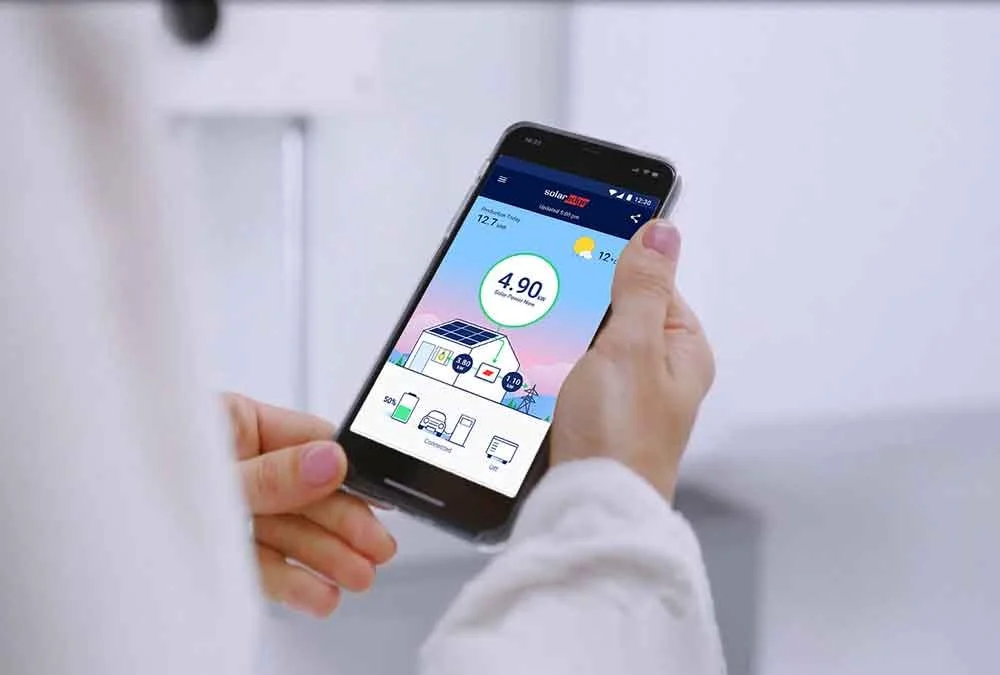 Person holding a smartphone showing a solar energy monitoring app with live generation stats.