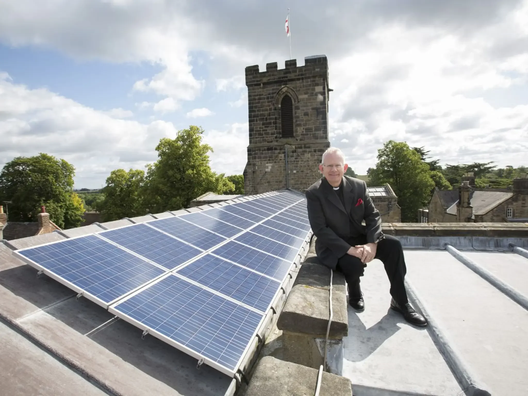 Solar panels installed on a church roof, with a church tower in the background.