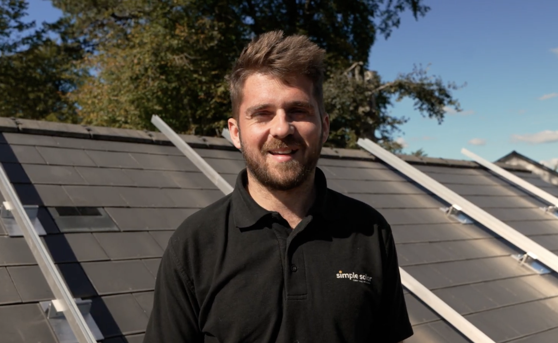 Simple Solar team member standing on a roof during a solar installation, with mounting rails visible behind him.