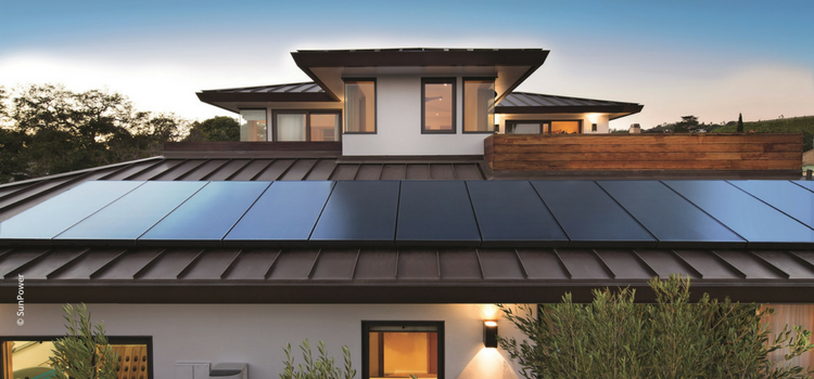 Modern home with sleek rooftop Sunpower performance 7 solar panels installed across a metal roof at sunset.