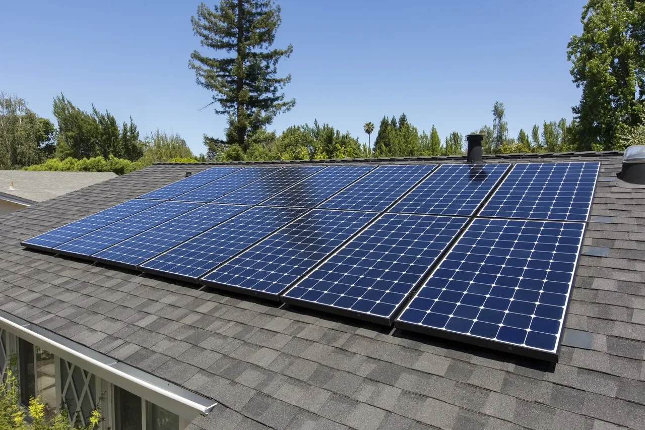 Array of glossy blue SunPower Maxeon 3 solar panels installed on a shingled residential rooftop under a clear blue sky with trees in the background.