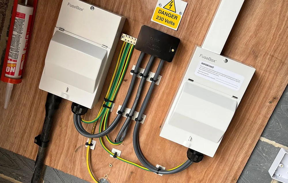 Two FuseBox electrical isolator units mounted on a board with conduit, earthing cables, and a “Danger 230 Volts” warning sign.