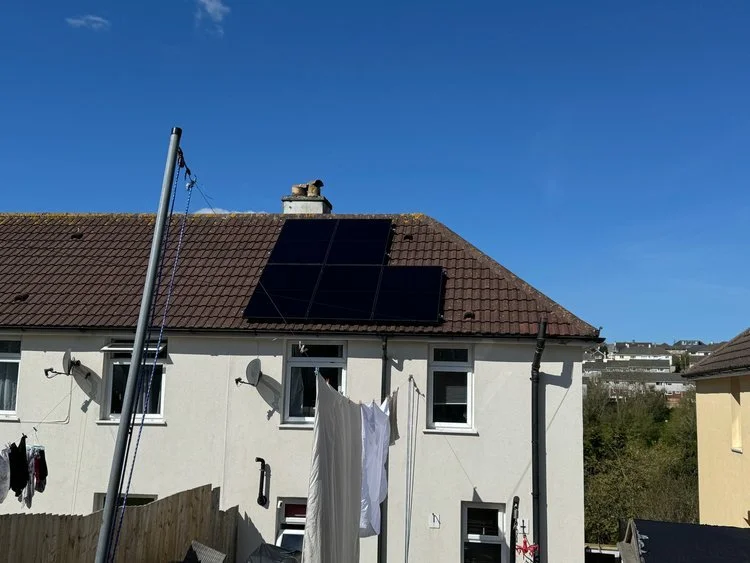 Solar panels installed on a pitched house roof under a clear blue sky.
