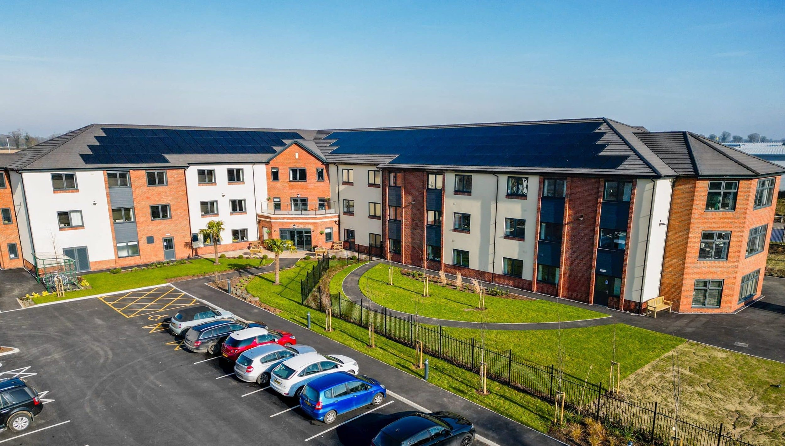 Apartment complex with large rooftop solar panel arrays, viewed from above with a car park in the foreground.