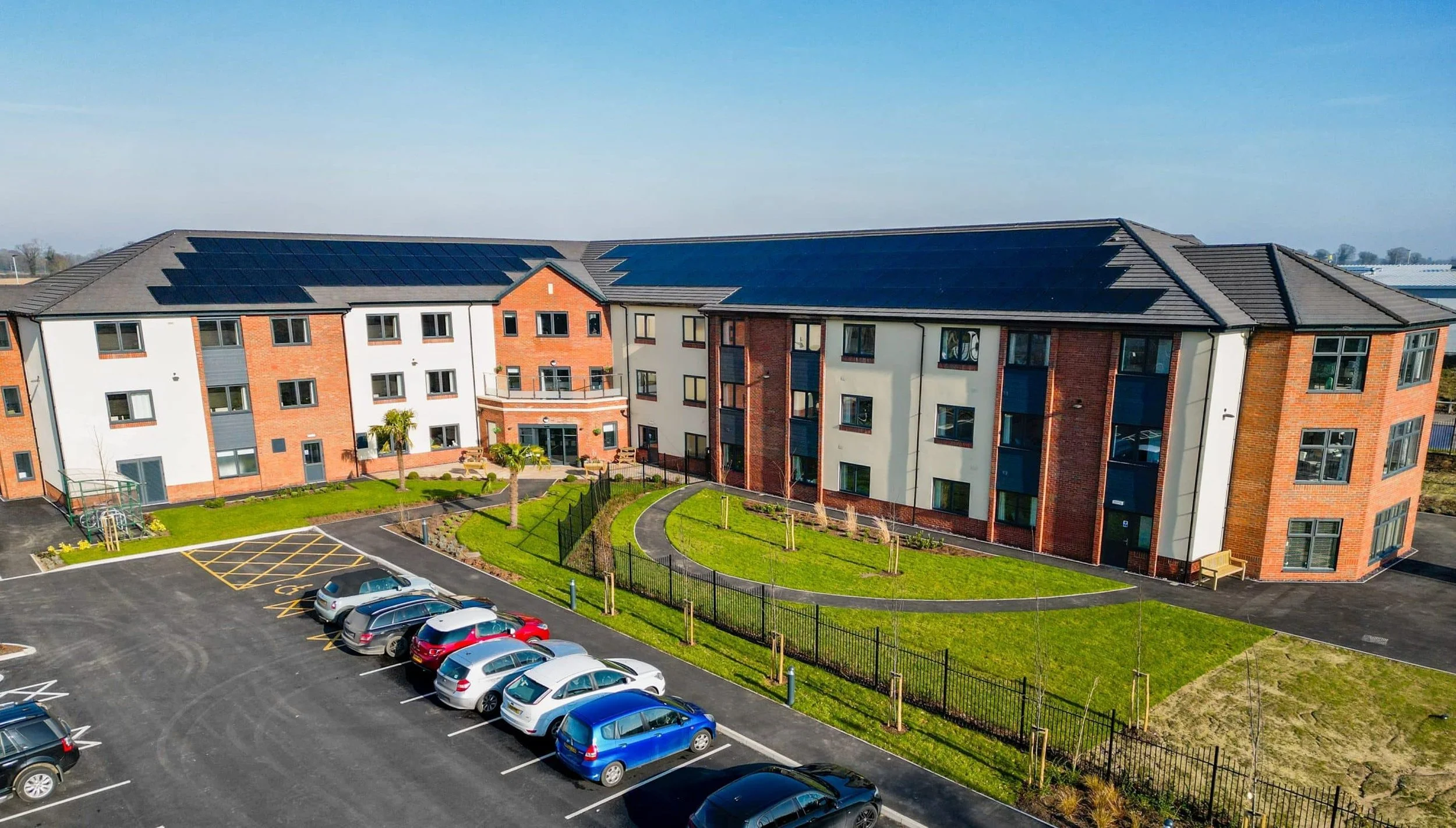 Large apartment complex with extensive rooftop solar panels, viewed from above with a car park in the foreground.