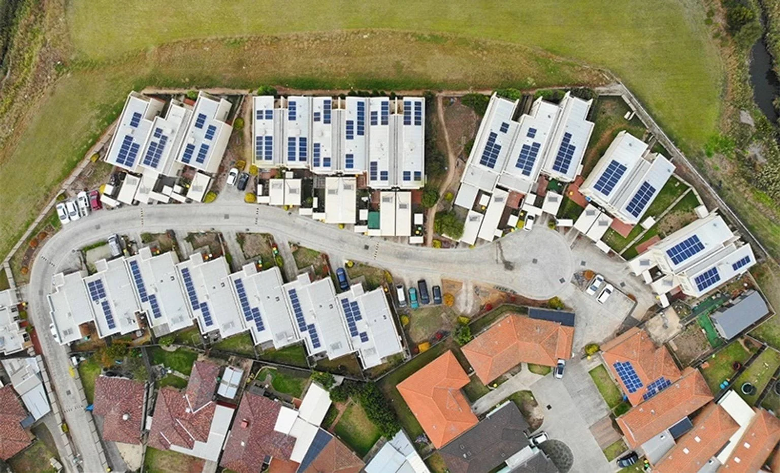 Aerial view of a residential neighbourhood with rows of modern white townhouses, most roofs equipped with solar panels