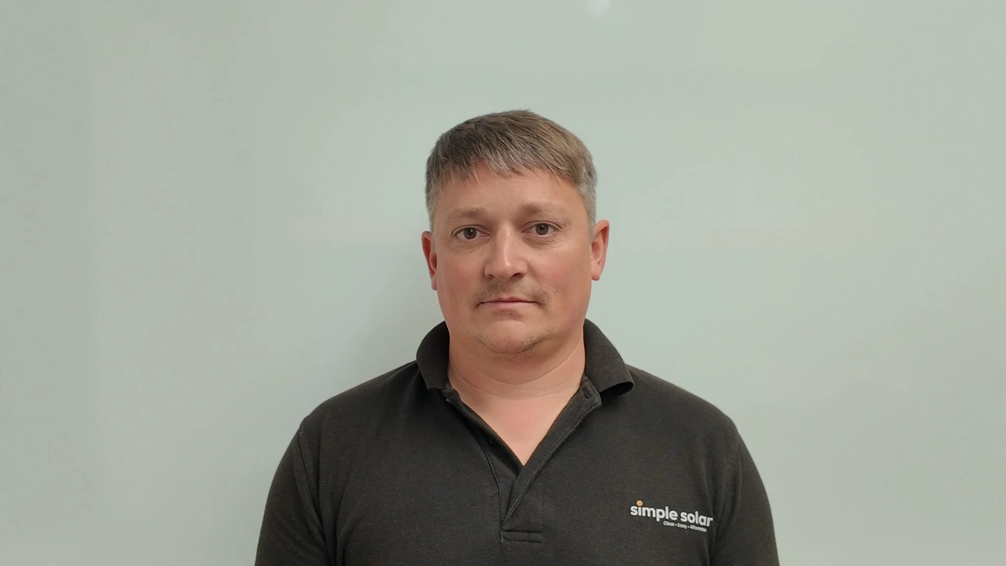 Headshot of Ben Quick wearing a Simple Solar black polo shirt.