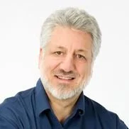 A smiling middle-aged man with gray hair and a beard, wearing a blue shirt.