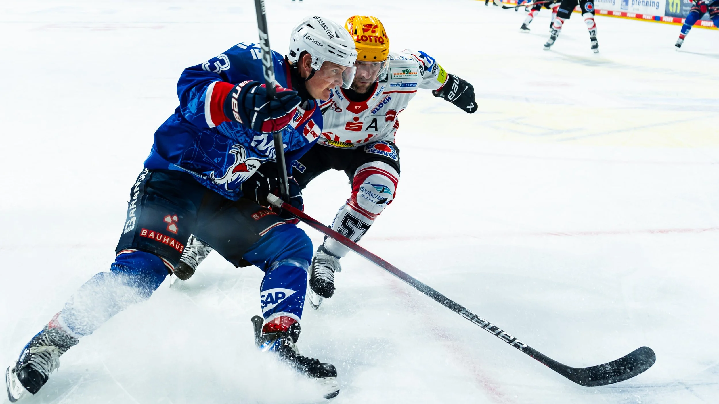 Eishockeyspiel mit zwei Spielern in Aktion auf dem Eis, einer in blauer Uniform und der andere in weißer Uniform, beide mit Helmen und Skates, beim Kampf um den Puck.