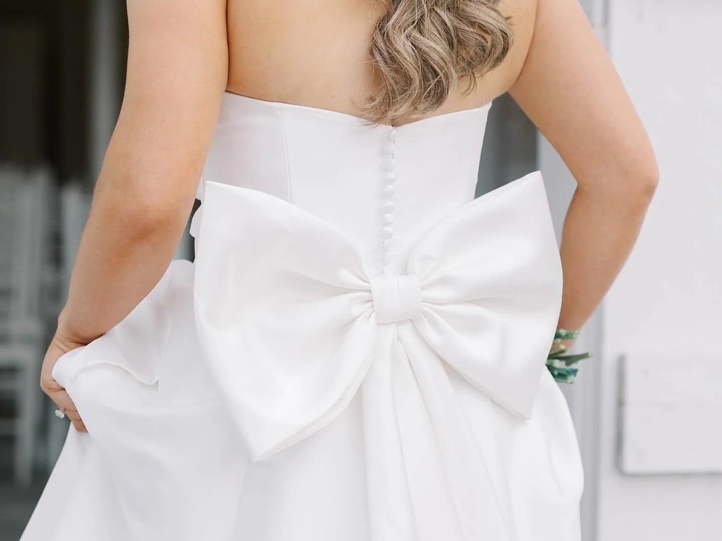Back view of a woman in a white strapless gown with a large satin bow at the waist.