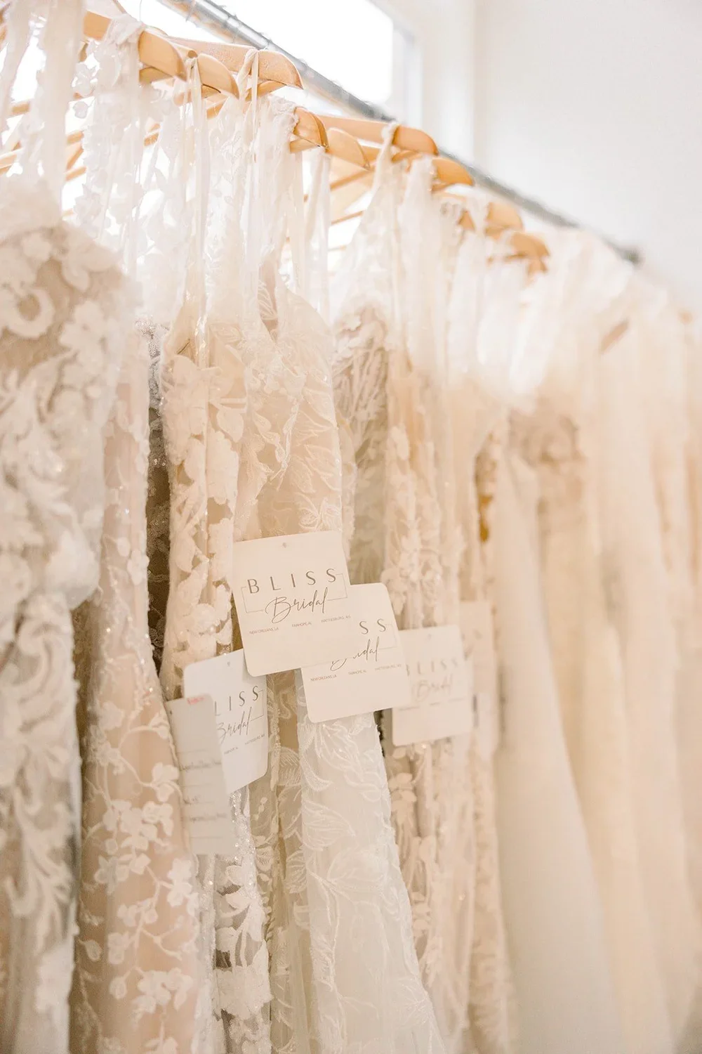 Multiple lace wedding dresses hanging on a clothing rack with tags labeled 'BLISS Bridal' and 'S s.'