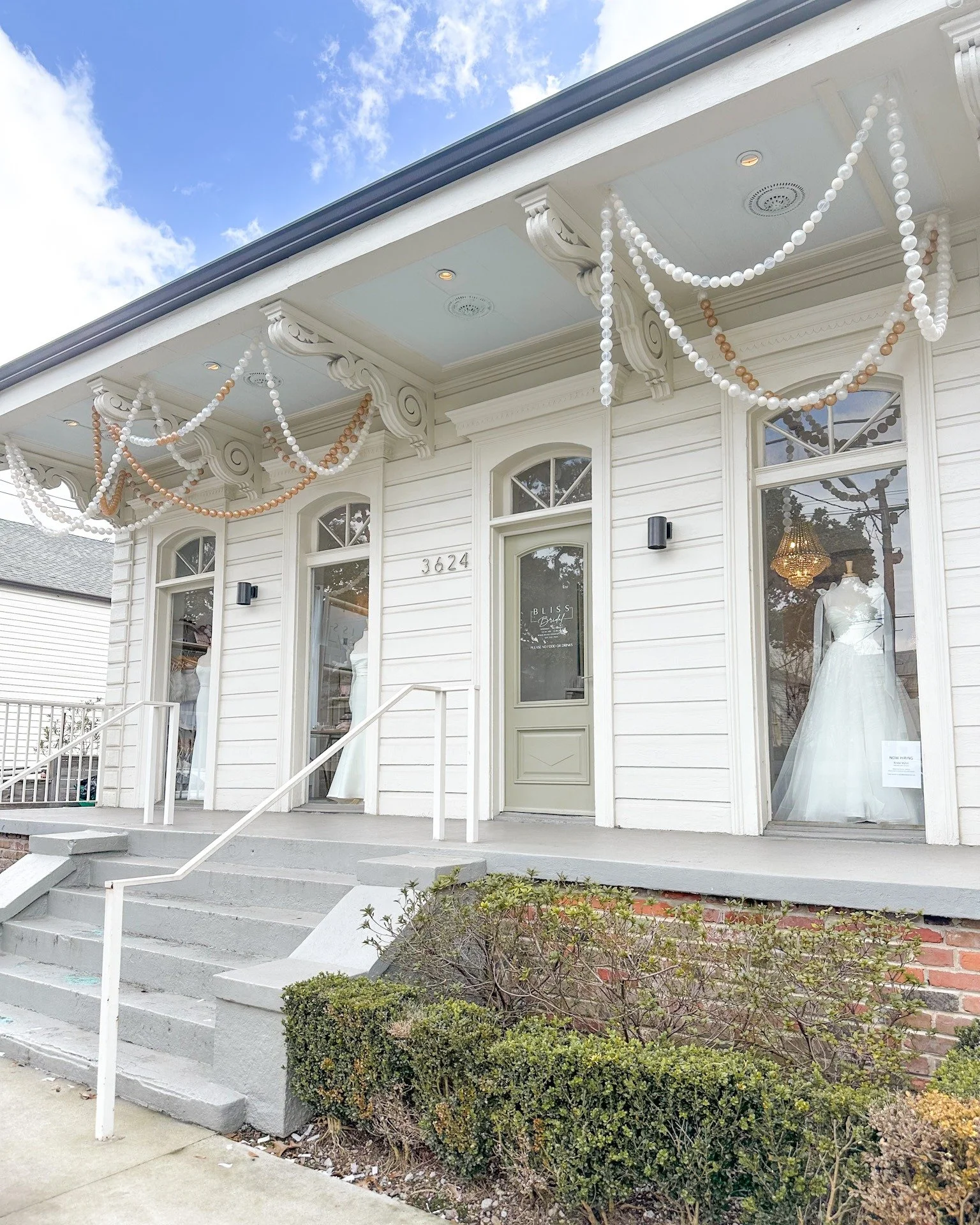 Exterior of a white building decorated with arrangements of white and brown beads, with large display windows showing white wedding dresses inside.