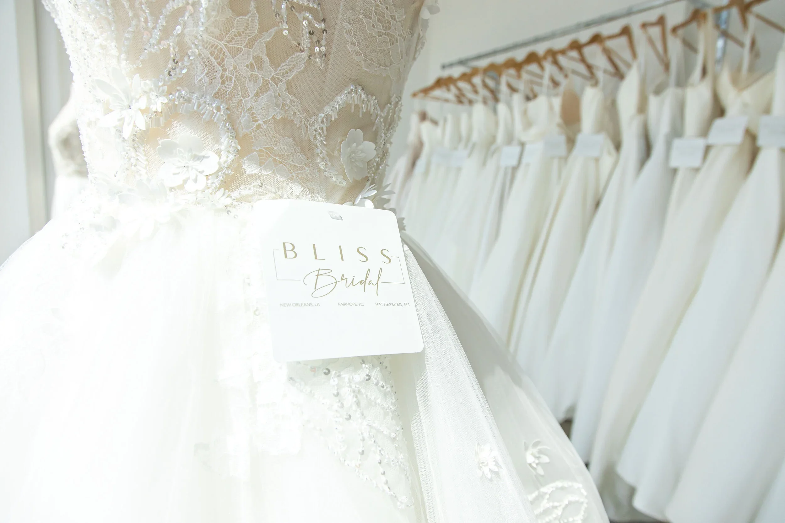 Wedding dress on a mannequin with a tag that reads 'Bliss Bridal' in a bridal shop.
