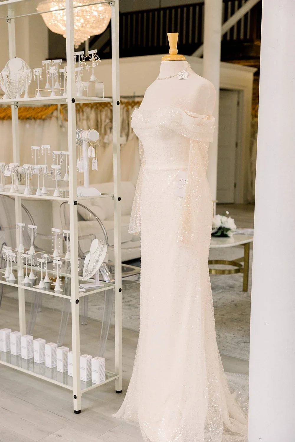 A mannequin wearing an off-shoulder, sparkly, cream-colored gown in a jewelry store.