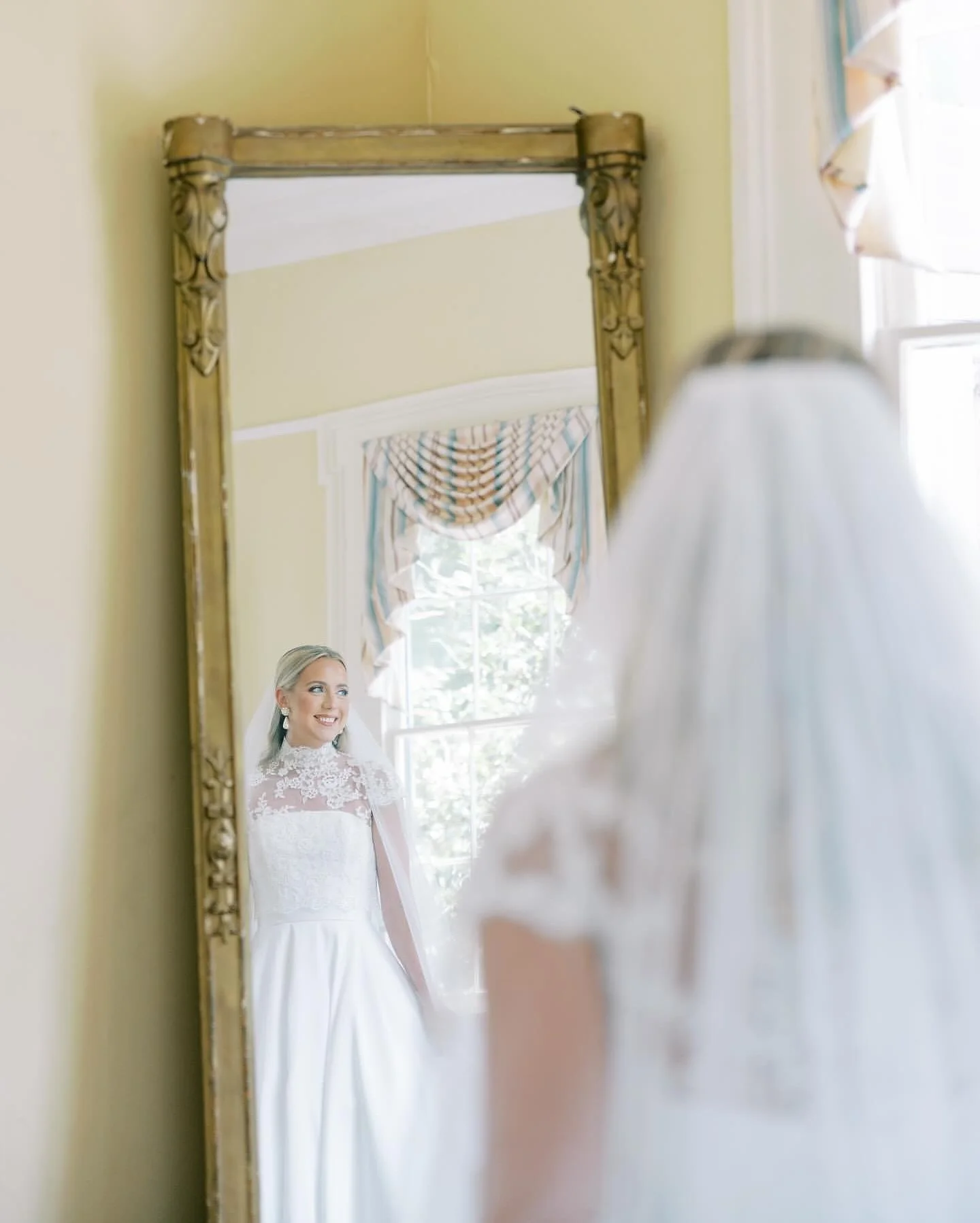 A bride in a white wedding dress looking at her reflection in a mirror.