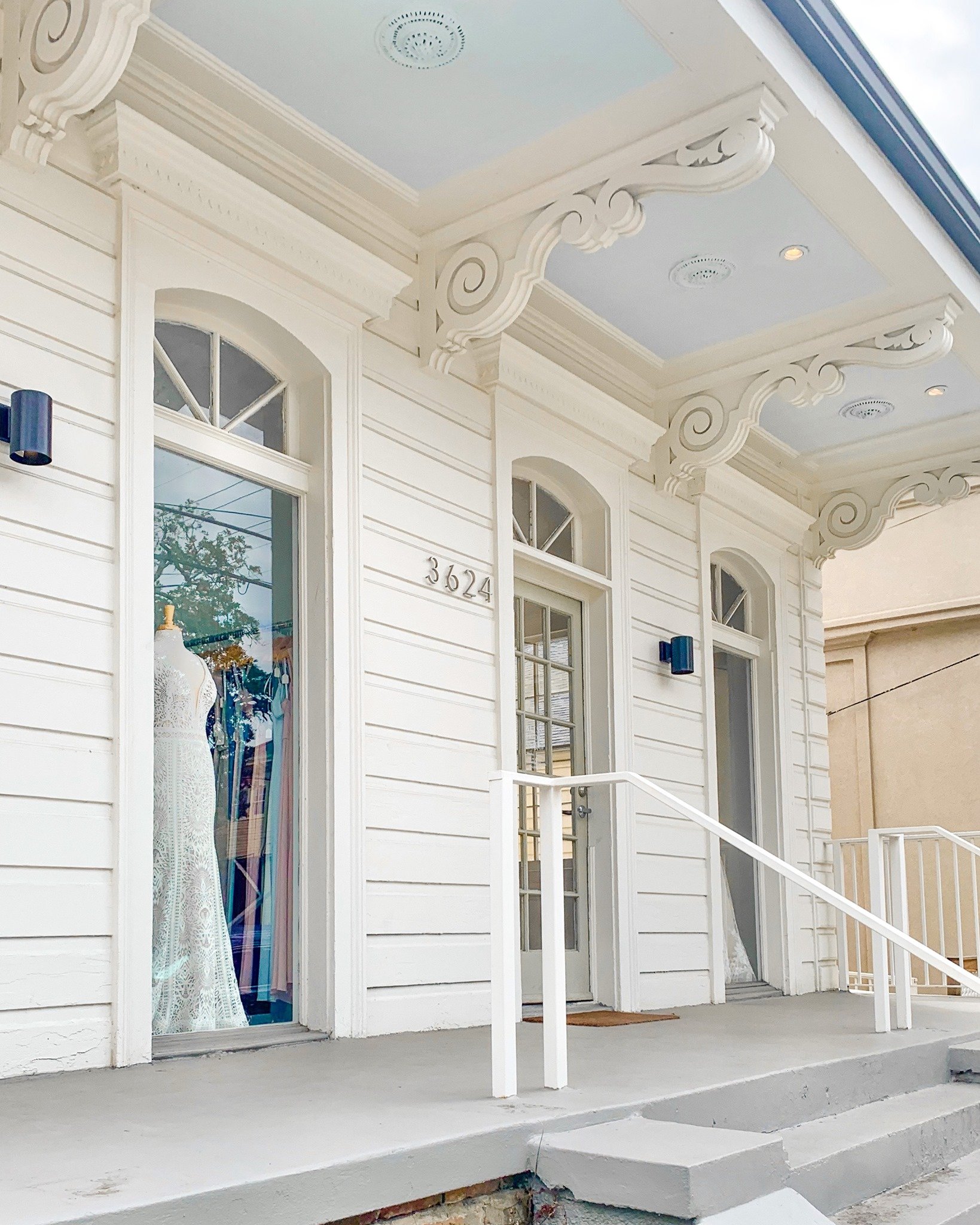 Exterior of a white building with a porch, ornate roof trim, and large windows displaying a mannequin in a lace dress, with house number 3624.