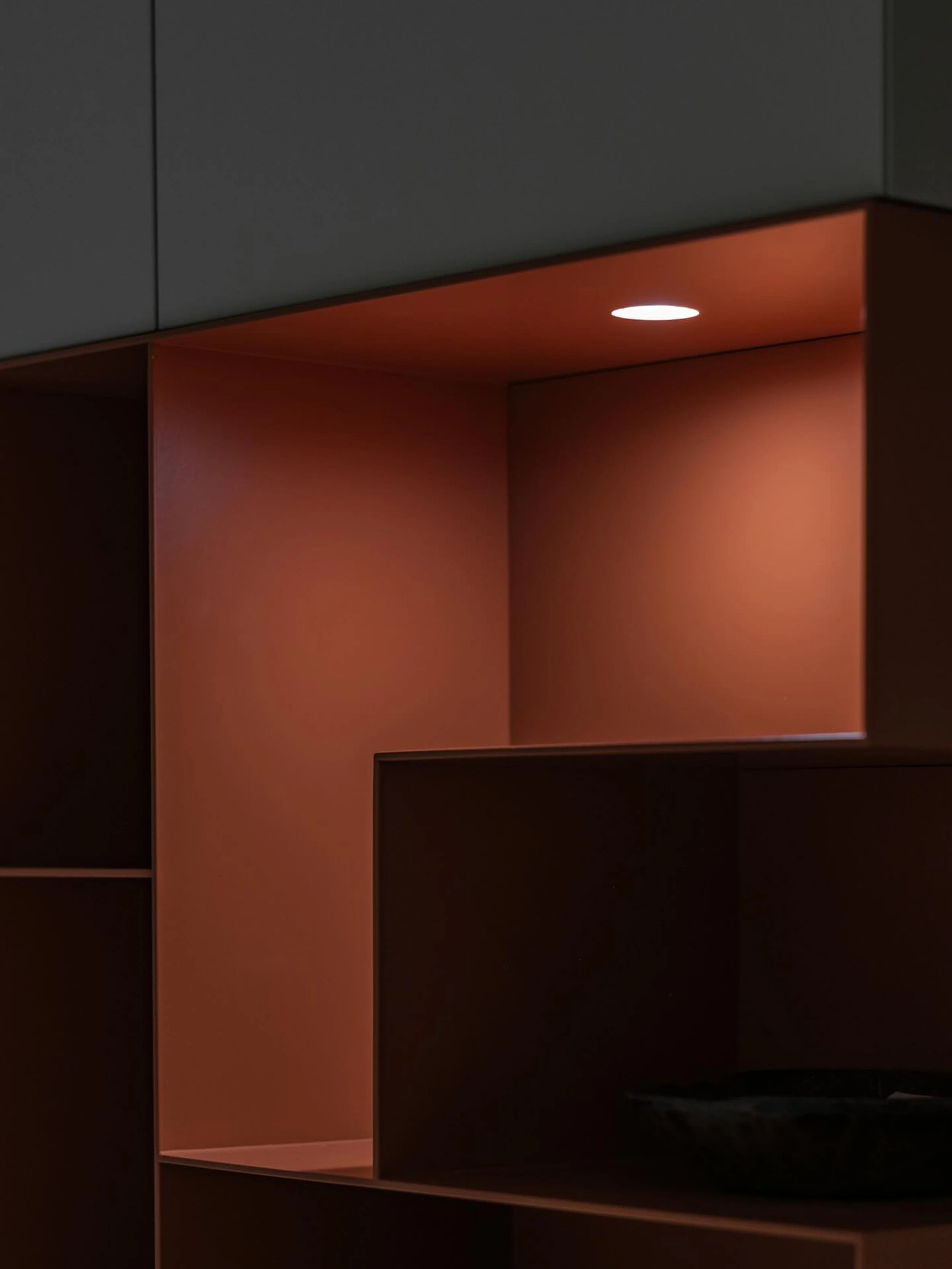 Ein moderner, dunkler Schrank mit offenen Fachbereichen, darunter ein beleuchteter Bereich mit warmem Licht innen.