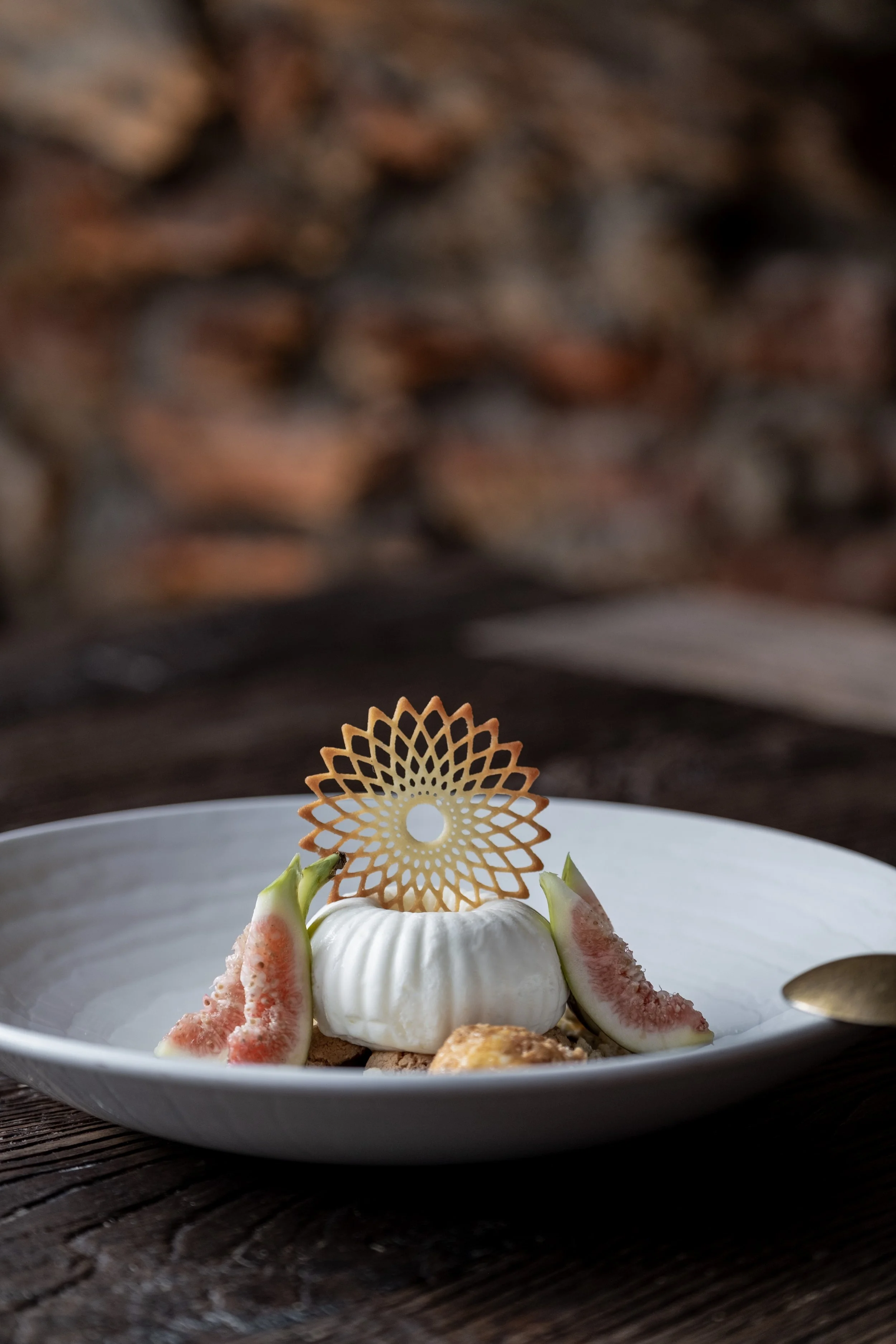 Dessert mit einer dekorativen Orangenschnecke, umgeben von Feigenstücken auf einem weißen Teller, auf einem dunklen Holztablett.