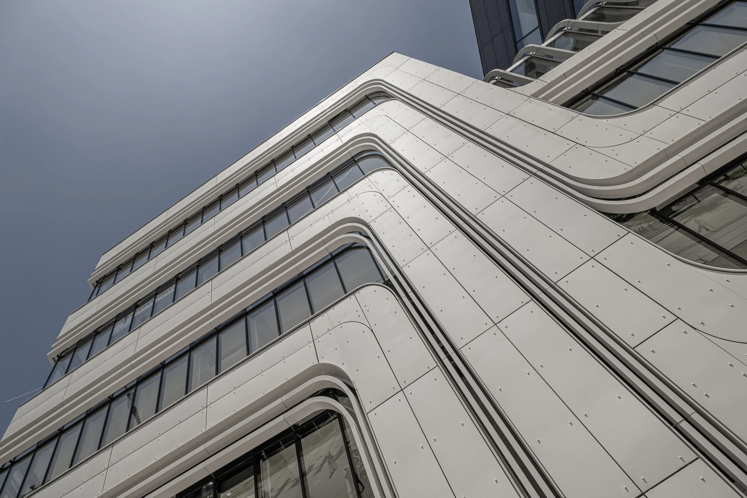 Moderne Gebäudefront mit geschwungenen Balkonen und großen Fenstern aus Glas, Blick nach oben gegen den Himmel.