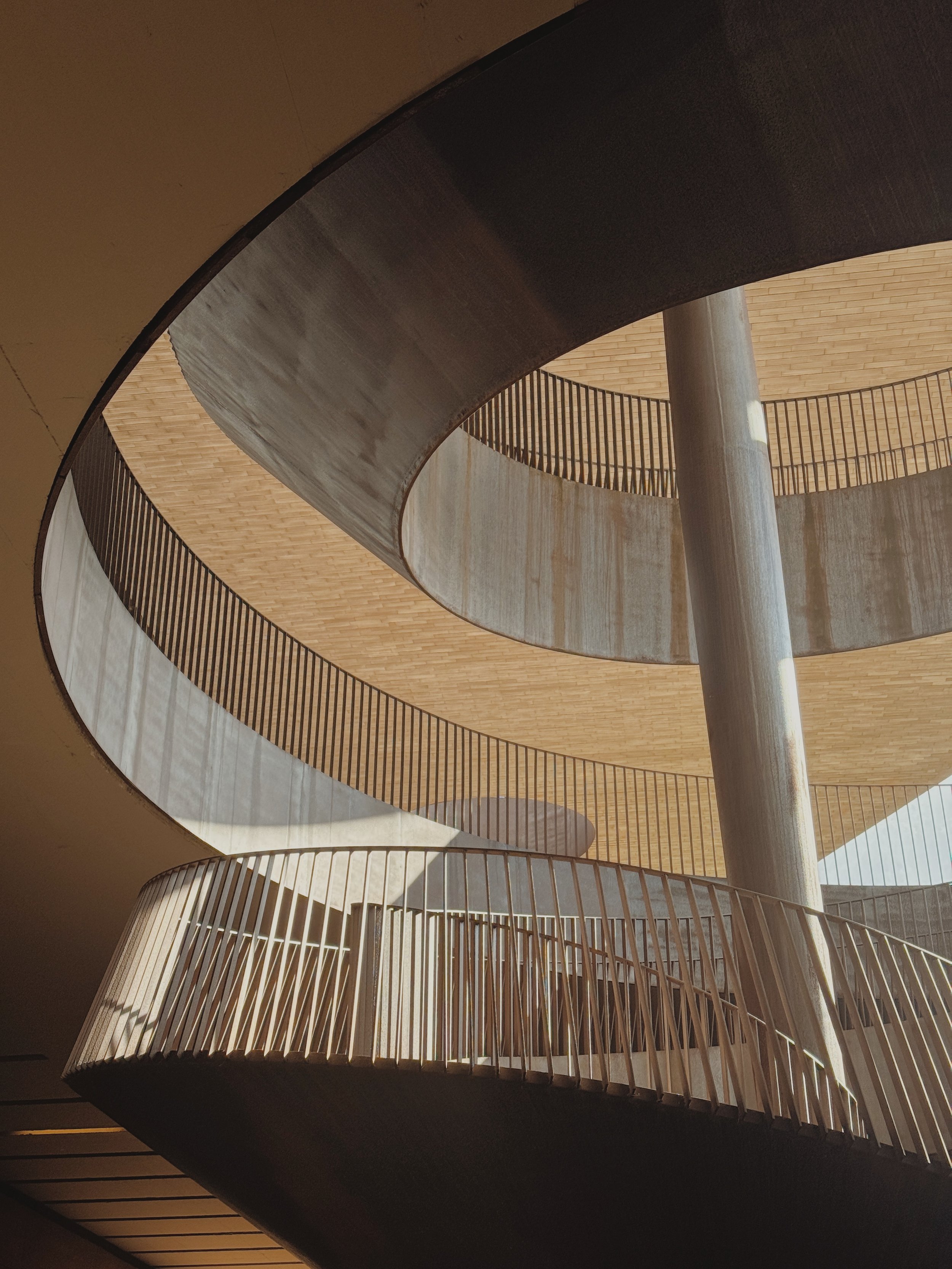Innenaufnahme einer spiralförmigen Rollladertreppe mit Holzgeländer und pfeiler, Licht fällt durch die Fensteröffnung, modernes architektonisches Design