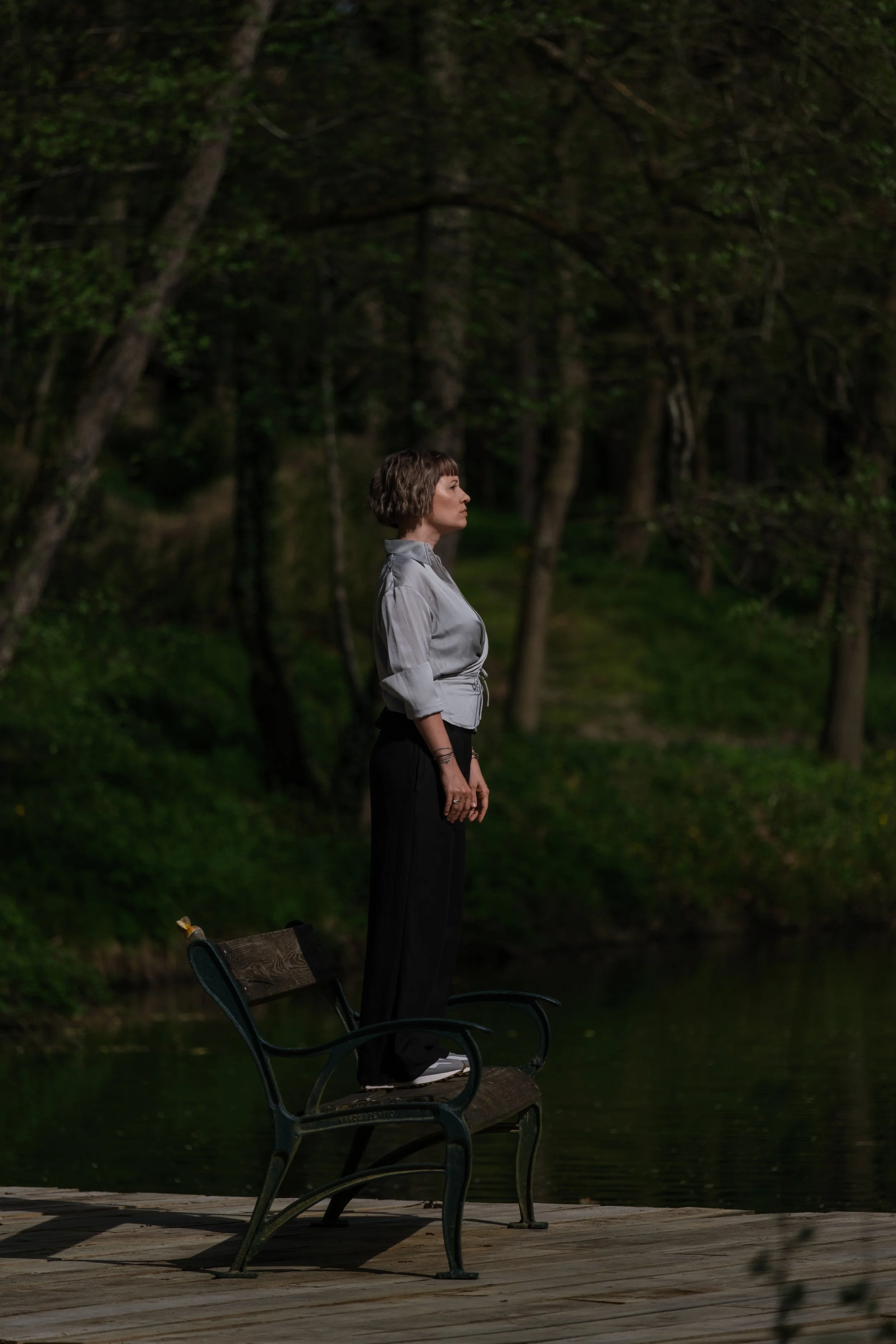 Frau steht auf einer Bank am Wasser, umgeben von Bäumen, bei Nacht.