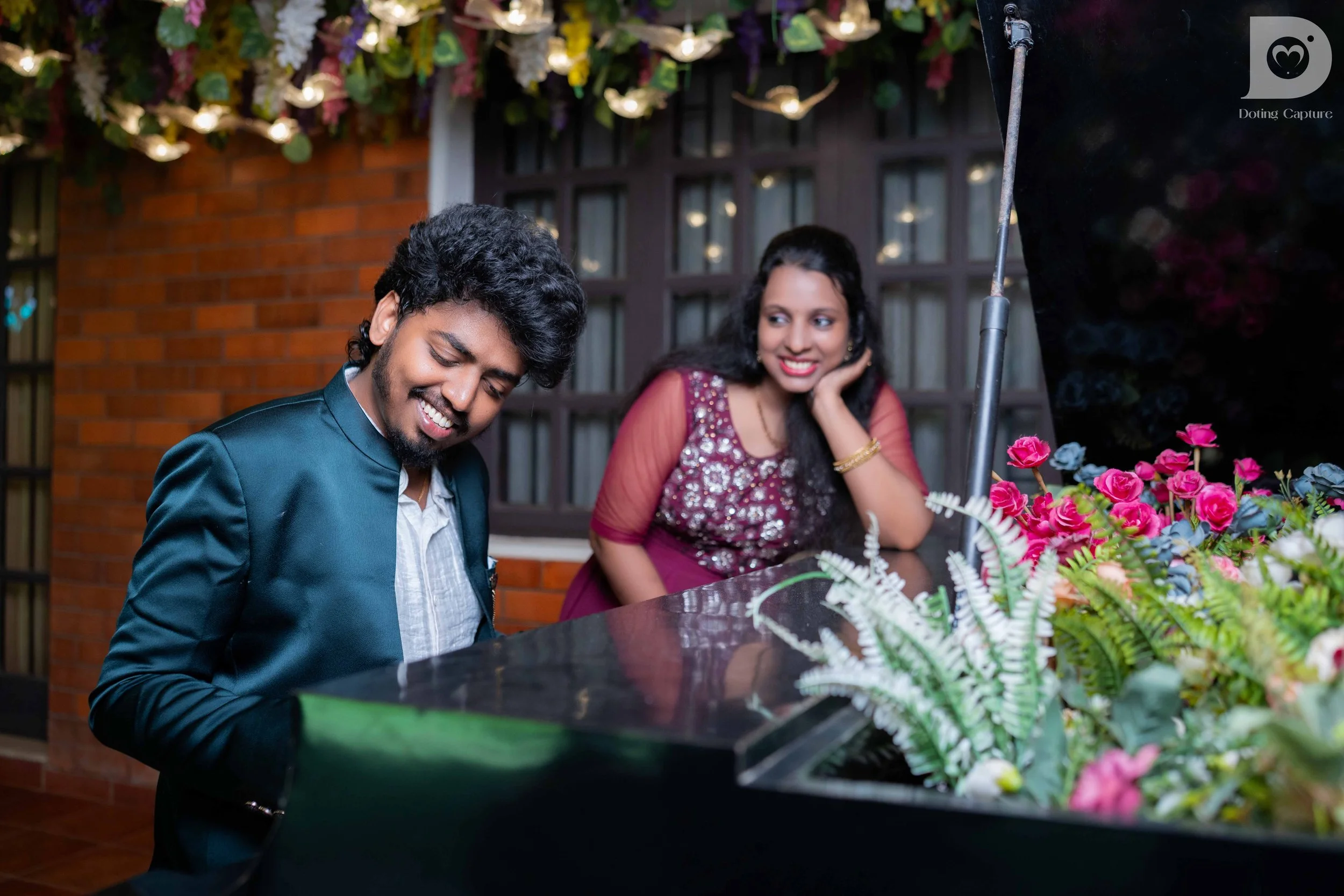 A man and woman enjoying playing a grand piano decorated with flowers at an outdoor event.