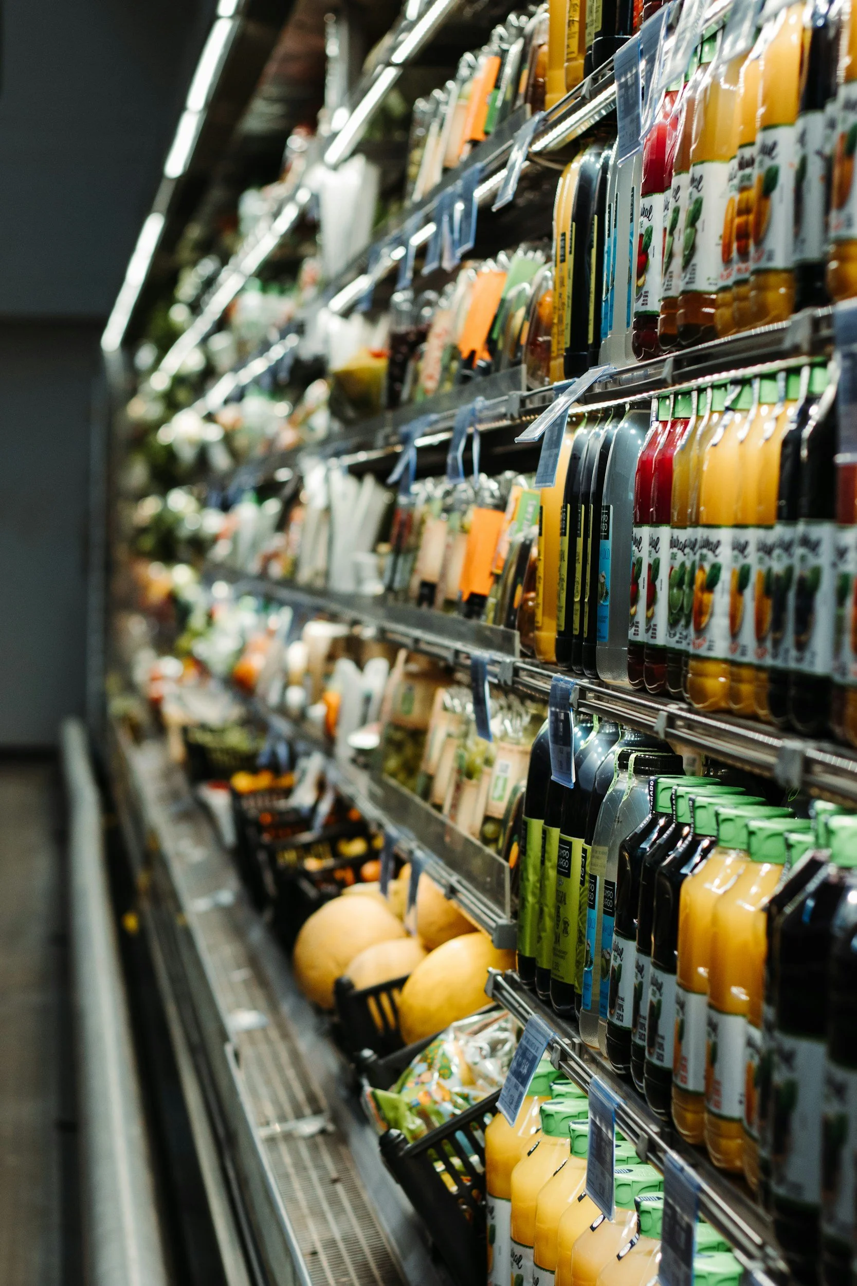 Grocery store aisle with bottles of juice, vegetables, and other produce on shelves.