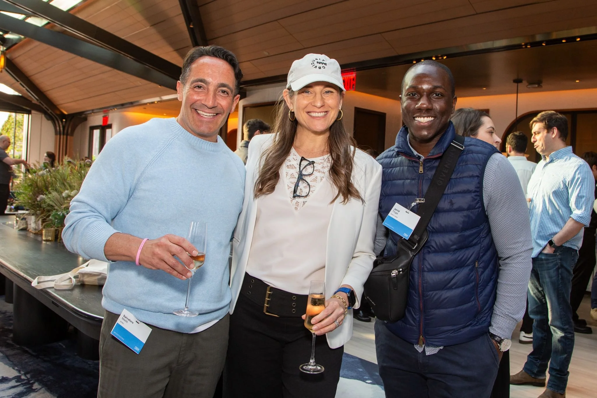 Three people posing together at a social event, holding glasses of wine, smiling.
