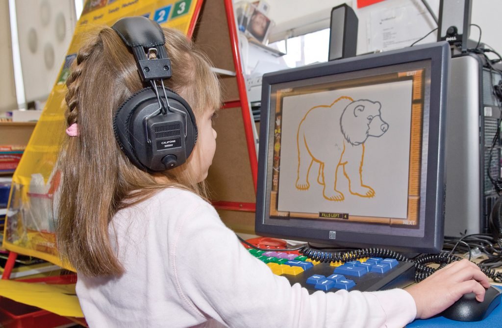 A young girl wearing headphones is using a computer to draw a bear on the screen.