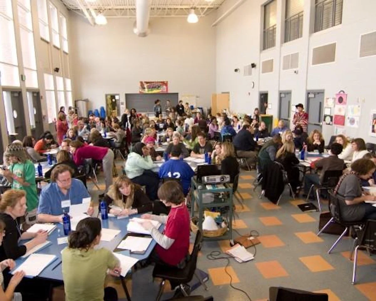 Large group of people seated at tables in a spacious room, likely participating in a meeting or conference.