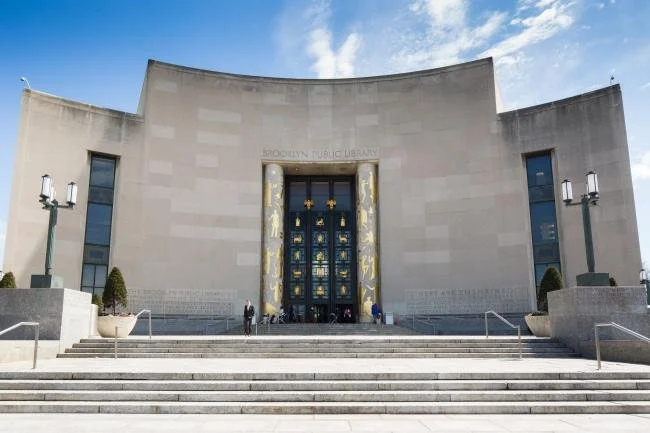 Front view of Brooklyn Public Library with steps leading up to entrance, glass doors, and lamps on either side