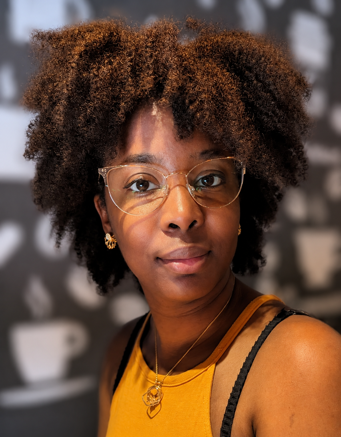Rhamah Norris, LMFT, LMHC sitting in front of a wall with coffee graphics. She is looking directly at the camera with a half-smile.